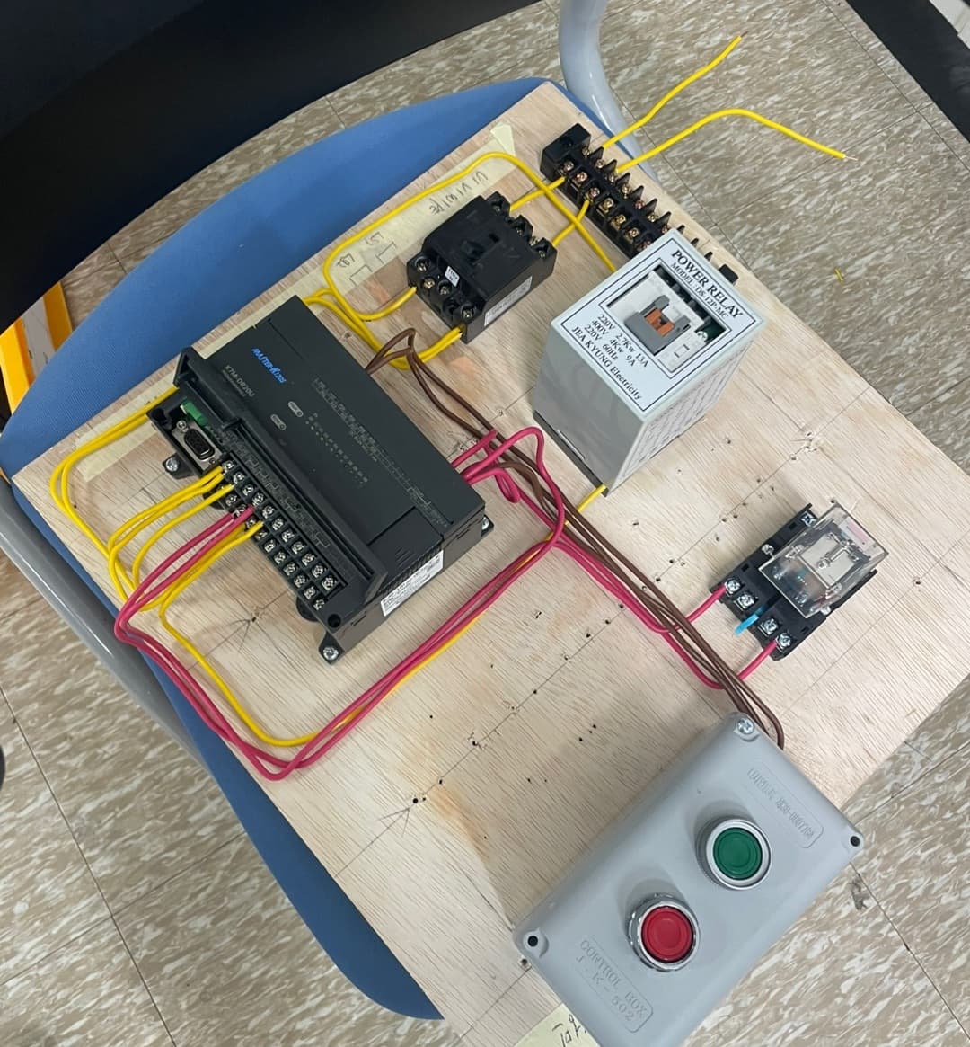 PLC wiring exercise on a wooden board, with relays, terminals, and start/stop buttons.